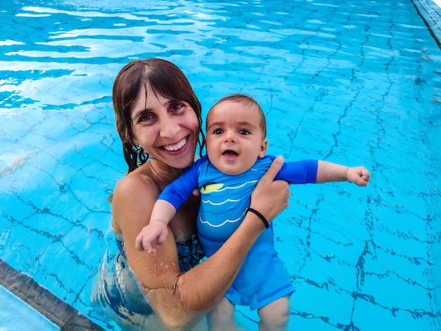 Uma jovem mãe caucasiana com seu bebê curtindo o verão tomando banho pela primeira vez em uma piscina