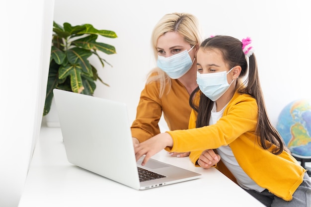 Uma jovem mãe caucasiana sorridente e uma filha pequena sentam-se em casa e usam um laptop moderno juntas. Mãe feliz e filha estudam conversa on-line em videochamada no computador.