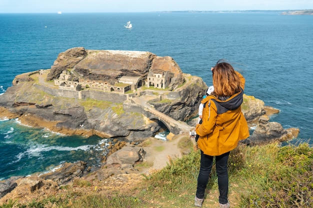 Foto uma jovem mãe com seu filho olhando para o fort des capucins, uma ilhota rochosa no topo de um penhasco na cidade de roscanvel, na península de crozon, na frança.