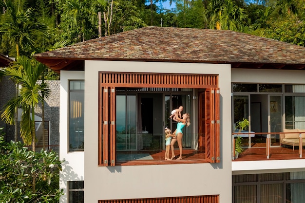 Uma jovem mãe com seus dois filhos está na varanda de uma villa tropical