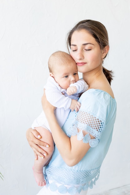 Uma jovem mãe com um recém-nascido o segura suavemente nos braços, abraçando-o e admirando-o em casa, o conceito de uma família feliz e o nascimento dos filhos.