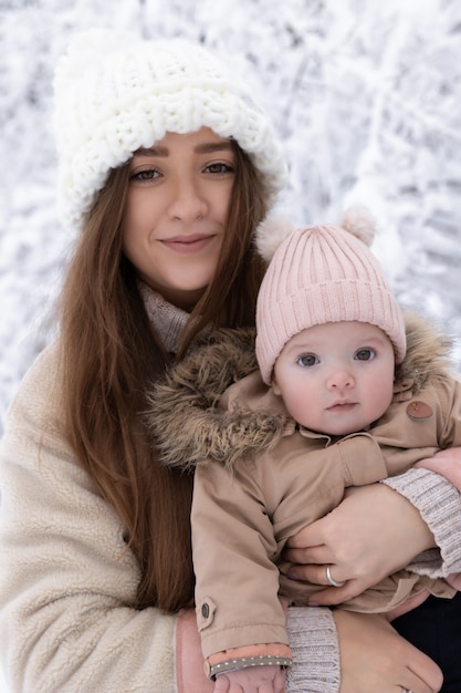 Uma jovem mãe com uma criança pequena brinca na neve, eles estão se divertindo e curtindo a queda de neve.