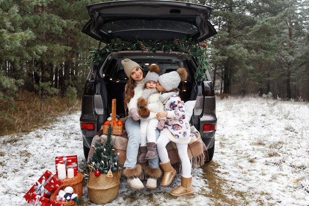 Uma jovem mãe e duas meninas estão sentadas no porta-malas de um carro