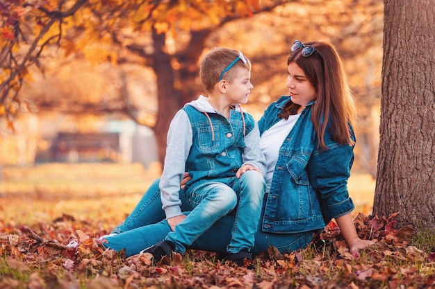 Uma jovem mãe e filho estão sentados em folhas douradas em um parque de outono o conceito de uma criança feliz