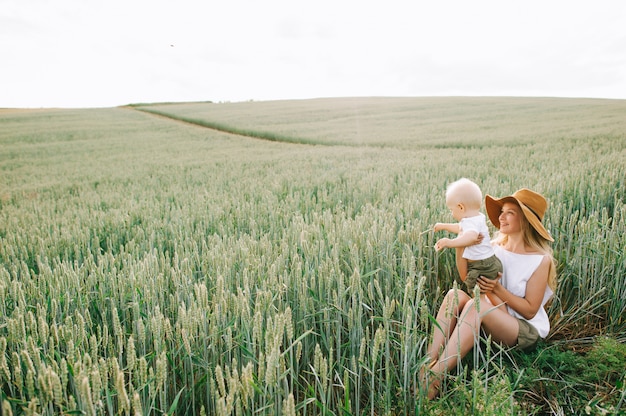 Uma jovem mãe e seu filho pequeno sentado perto do trigo em um fundo verde