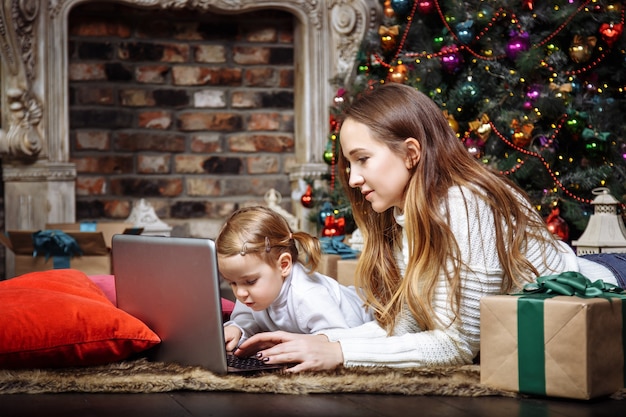 Uma jovem mãe e sua filha usando um laptop perto da árvore de Natal