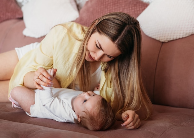 Uma jovem mãe está deitada em uma cama com uma filha recém-nascida. Comunicação, olhando um para o outro