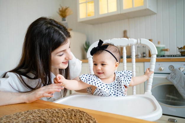 Foto uma jovem mãe feliz está brincando com seu bebê de 9 meses na cozinha de uma casa de campo