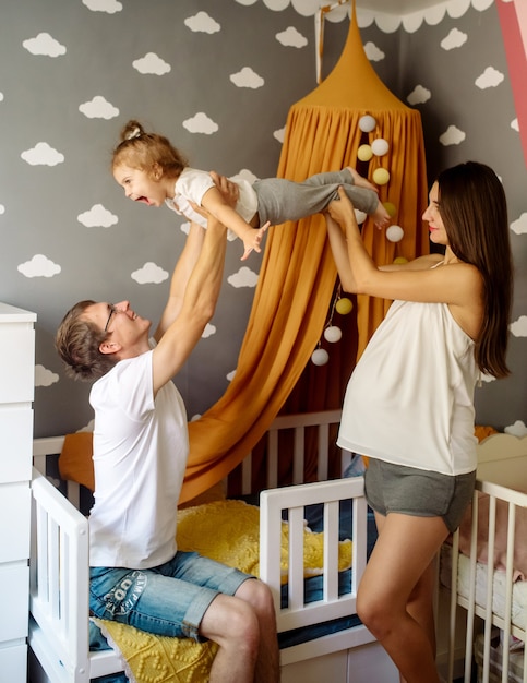 Uma jovem mãe grávida e um lindo pai de óculos brincam com a filha