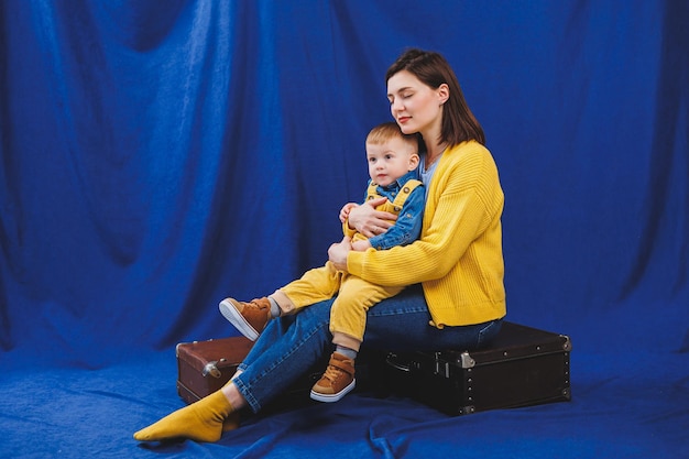 Uma jovem mãe senta-se com um filho de 3 anos em seus braços relações familiares com uma criança Educação infantil Mãe com filho em um fundo azul