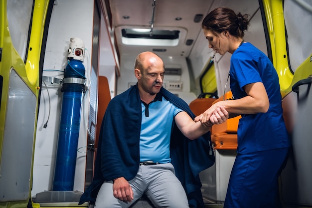 Uma jovem médica verificando a mão traumatizada de seu paciente em uma ambulância.