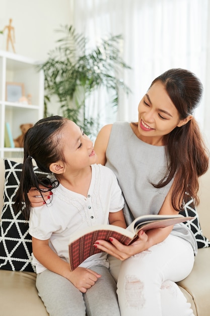 Uma jovem mesquinha e sua filha pré-adolescente lendo um livro juntas quando estão sentadas no sofá da sala de estar