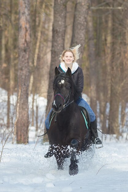 Uma jovem montando um cavalo preto na floresta de neve