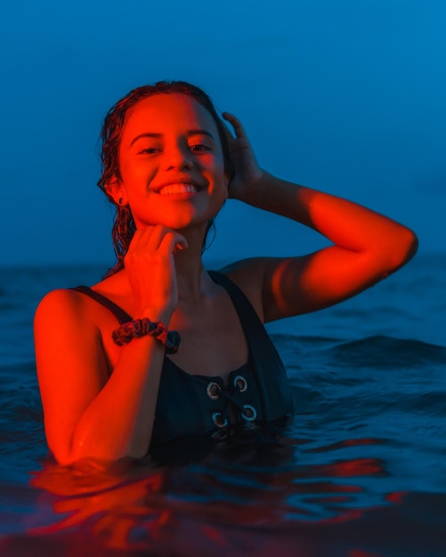 Uma jovem morena caucasiana tomando banho à noite no mar com uma luz vermelha iluminada