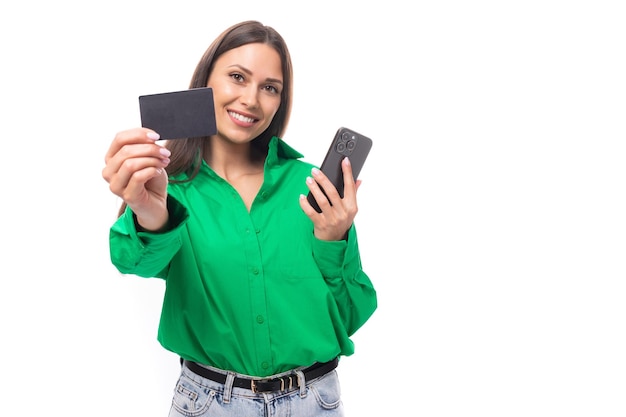 Uma jovem morena europeia esbelta sorridente com maquiagem em uma camisa verde mostra um banco