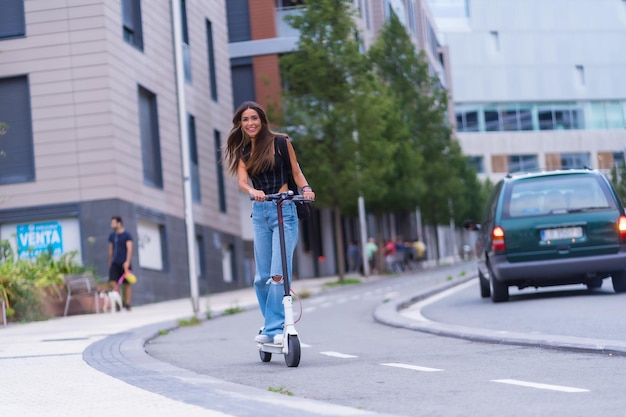 Uma jovem morena se movendo na cidade com uma scooter elétrica sorrindo ao longo da ciclovia