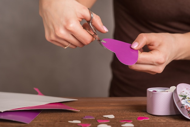 Uma jovem mostra como cortar um coração de papelão colorido com uma tesoura. Uma lição de criatividade. Processo artístico