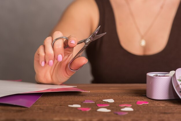 Uma jovem mostra como cortar um coração de papelão colorido com uma tesoura. Uma lição de criatividade. Processo artístico