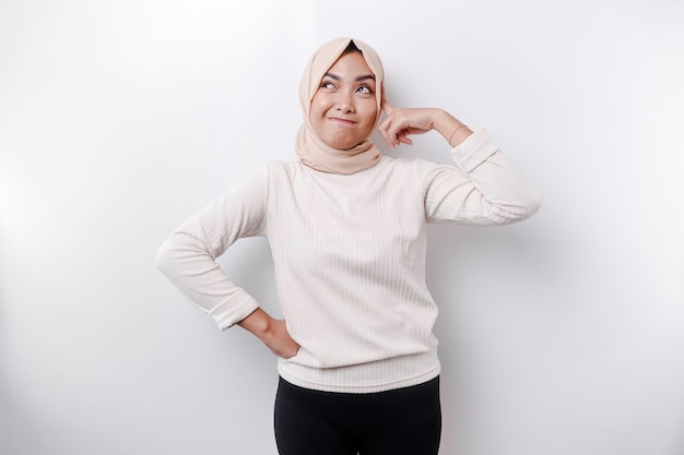 Uma jovem muçulmana asiática pensativa usando lenço na cabeça enquanto olha de lado isolada por um fundo branco