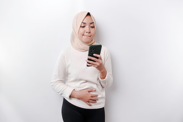 Uma jovem muçulmana asiática pensativa usando um hijab e segurando o queixo enquanto fala ao telefone isolada por um fundo branco