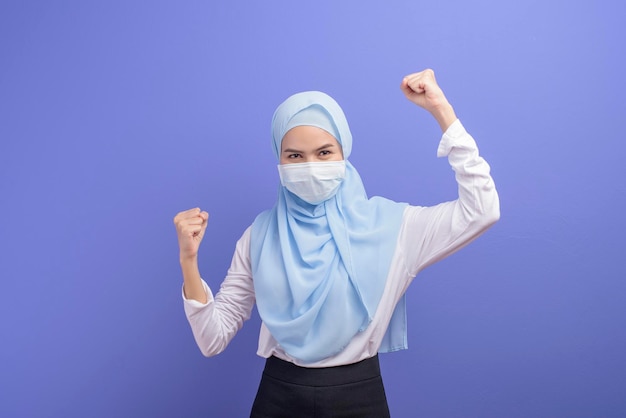 Uma jovem muçulmana com hijab usando uma máscara cirúrgica sobre estúdio de fundo azul.