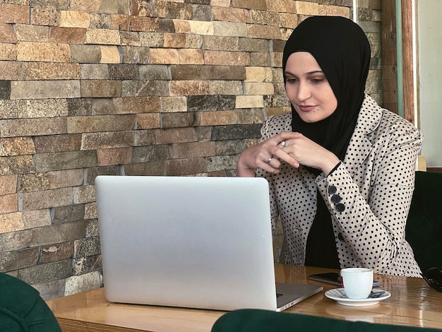 Uma jovem muçulmana feliz em hijab trabalhando em um laptop no restaurante café