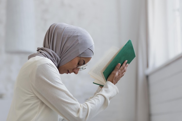 Uma jovem muçulmana linda em um hijab está rezando em casa sentada perto da janela