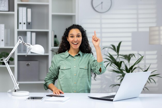 Uma jovem muçulmana senta-se no escritório em uma mesa com um laptop olha para a câmera aponta sua