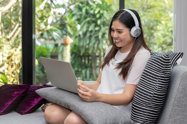 Foto uma jovem muito sorridente usa fones de ouvido sentado no sofá e usando no laptop