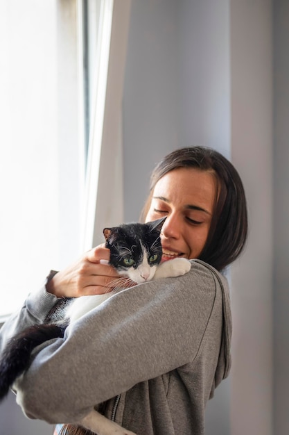 Uma jovem mulher abraça e brinca com seu gato preto e branco enquanto está em casa