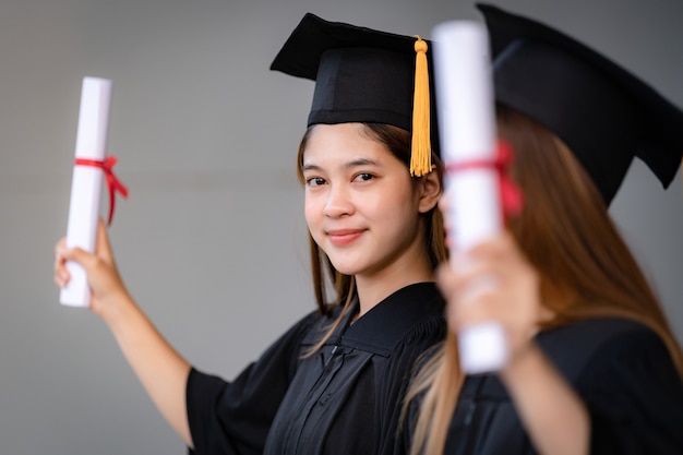 Uma jovem mulher asiática feliz, graduada em vestido de formatura e mortarboard, possui um certificado de graduação que comemora o desempenho educacional no campus da universidade. Foto de estoque de educação