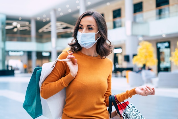 Uma jovem mulher bonita com máscara de segurança médica com sacolas de compras está andando no shopping na sexta-feira negra