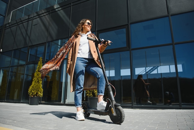 Uma jovem mulher bonita com um casaco a sorrir e a conduzir uma scooter eléctrica para o trabalho