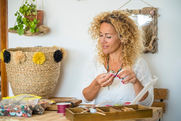 Uma jovem mulher bonita em casa fazendo criações de joias feitas à mão com miçangas