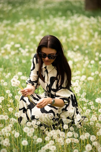 Uma jovem mulher bonita em um gramado com dentes-de-leão soprando fazendo um desejo