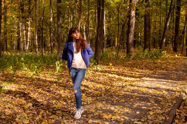 Uma jovem mulher bonita no parque de outono e o sol brilha no fundo das árvores amarelas