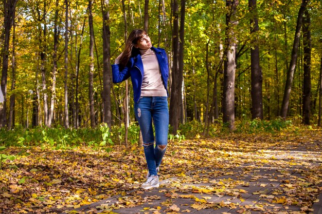 Uma jovem mulher bonita no parque de outono e o sol brilha no fundo das árvores amarelas