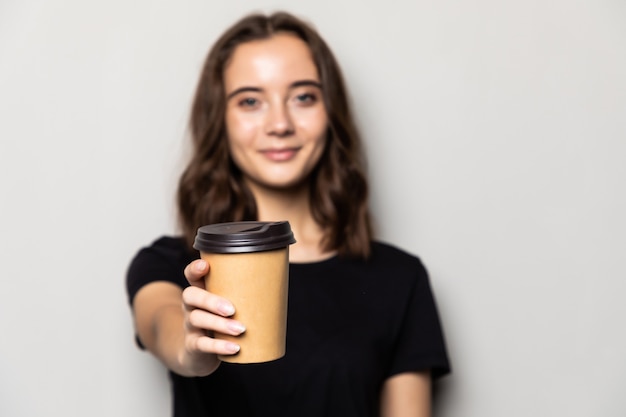 Uma jovem mulher bonita oferece uma xícara de café branca isolada na parede cinza