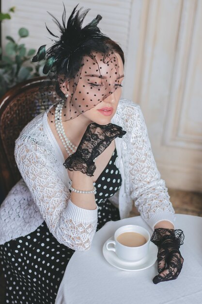 Uma jovem mulher bonita vestida em estilo retro está sentada no café da rua com uma xícara de café