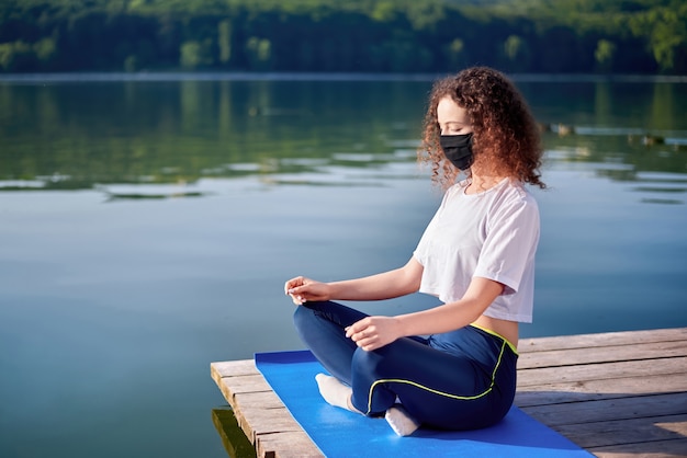 Foto uma jovem mulher com cabelos cacheados, fazendo yoga fora