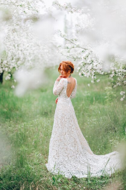 Uma jovem mulher com um vestido de noiva está em um jardim florido de primavera