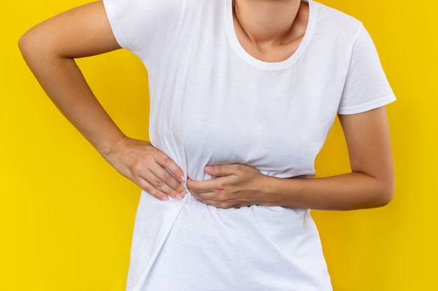 Uma jovem mulher com uma camiseta branca segurando o lado do corpo com as mãos isoladas em um fundo de cor amarela