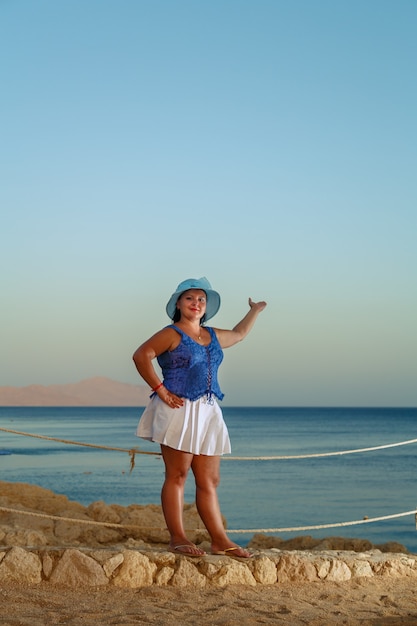 Uma jovem mulher com uma saia branca e um chapéu de sol à beira-mar parece de altura.