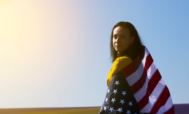 Uma jovem mulher de cabelos escuros segurando a bandeira dos Estados Unidos da América contra o céu ensolarado. Dia do Memorial e conceito do Dia da Independência dos EUA.