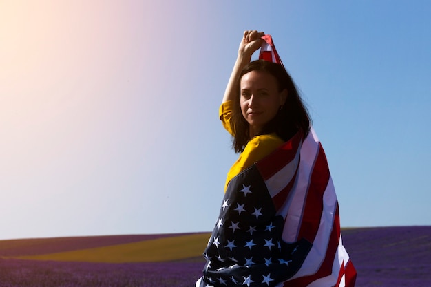 Uma jovem mulher de cabelos escuros segurando a bandeira dos Estados Unidos da América contra o céu ensolarado. Dia do Memorial e conceito do Dia da Independência dos EUA.