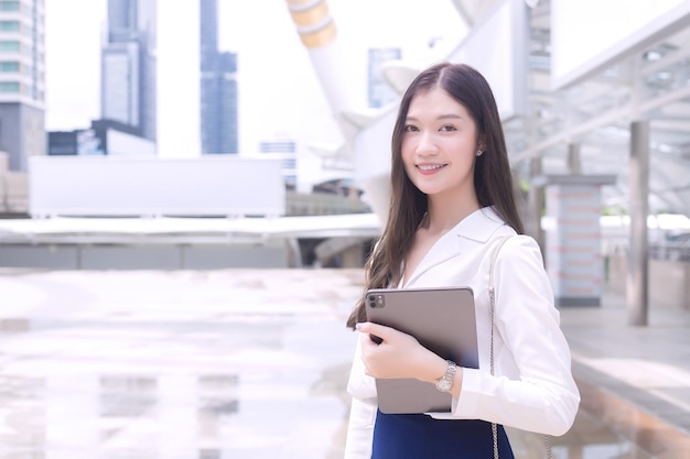 Uma jovem mulher de negócios asiática está indo para o escritório ou local de trabalho, segurando um bloco de notas nas mãos