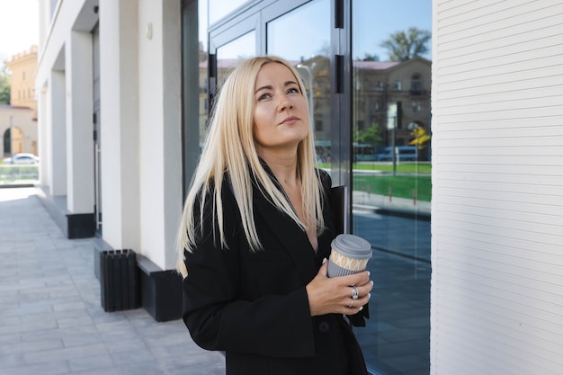 Uma jovem mulher em um terno elegante com um laptop e uma xícara de café no fundo de um centro de negócios