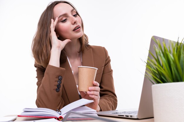 Uma jovem mulher em um terno marrom bebe café no local de trabalho. Isolado