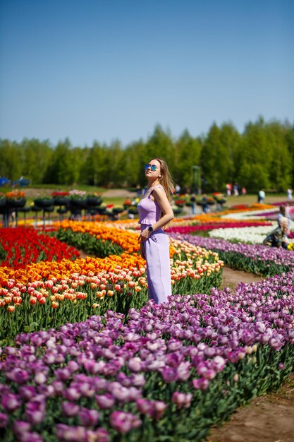 Uma jovem mulher em um terno rosa está em um campo florido de tulipas. Tempo de primavera