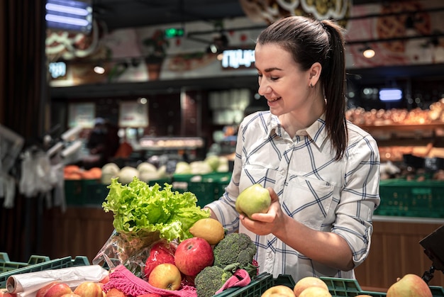 Uma jovem mulher escolhe frutas e legumes em um supermercado